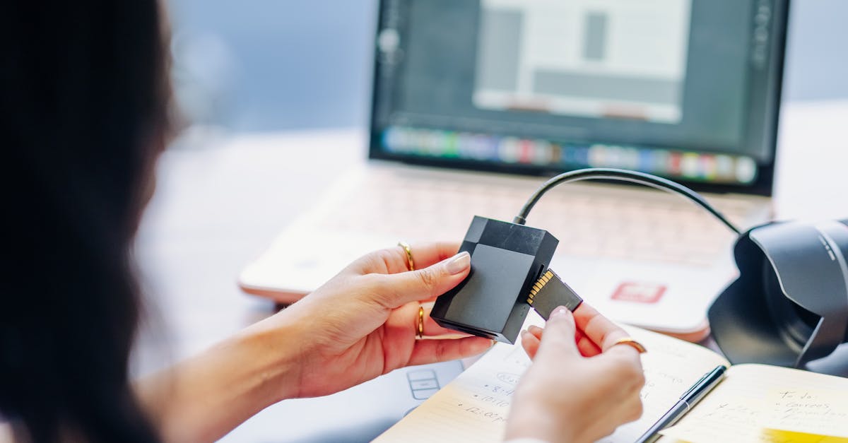 Person inserting an SD card into a USB card reader connected to a laptop at a desk